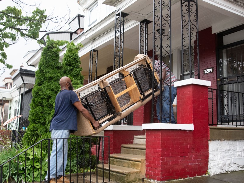 on the front porch of a home, two workers, both men, removing a couch