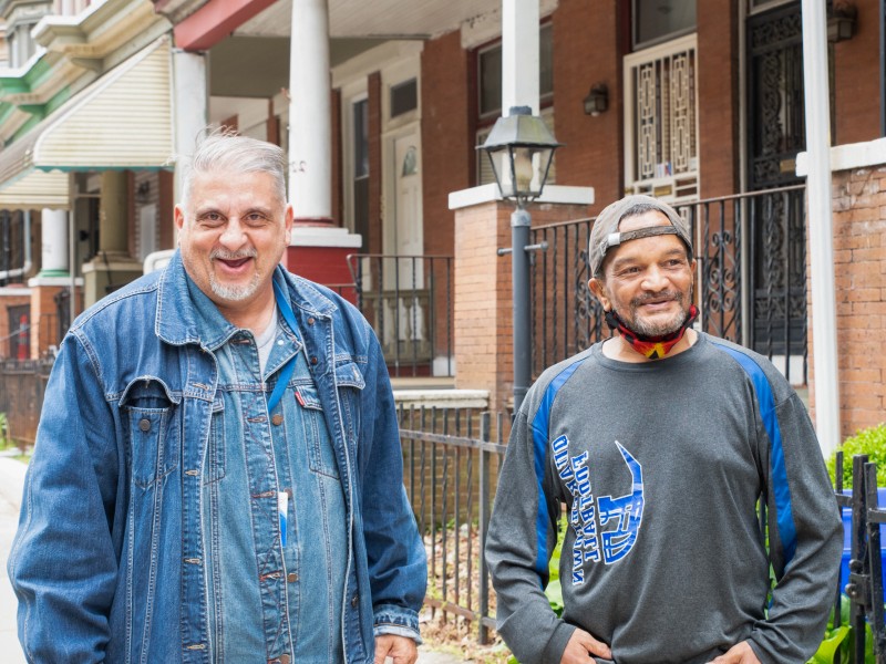 two people smiling on a sidewalk