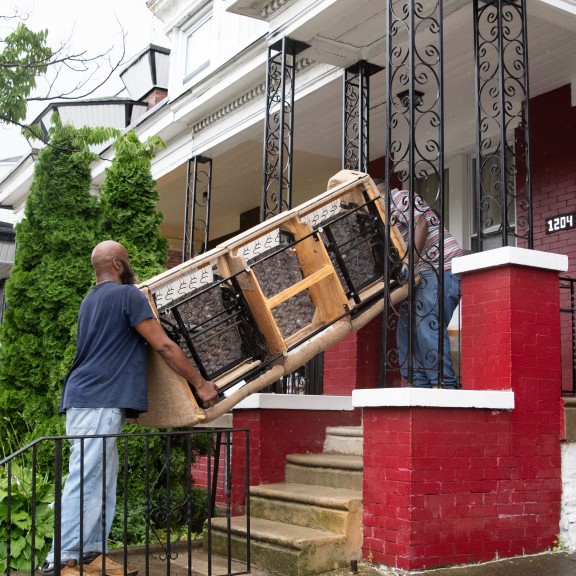 on the front porch of a home, two workers, both men, removing a couch