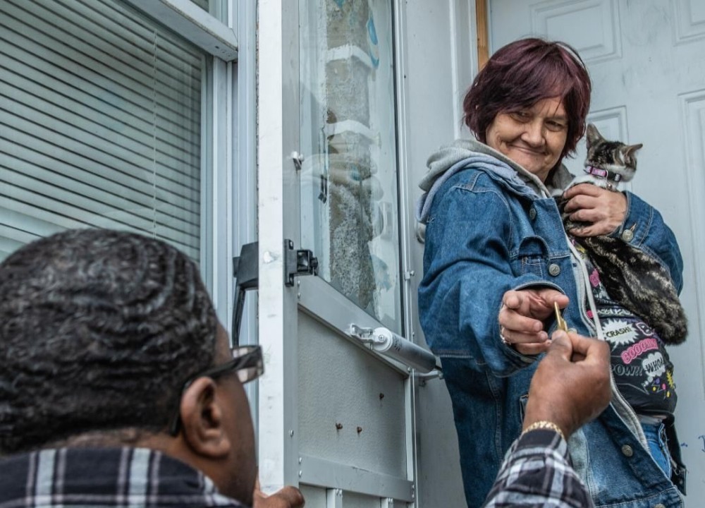 A person hands a house key to a smiling person holding a cat