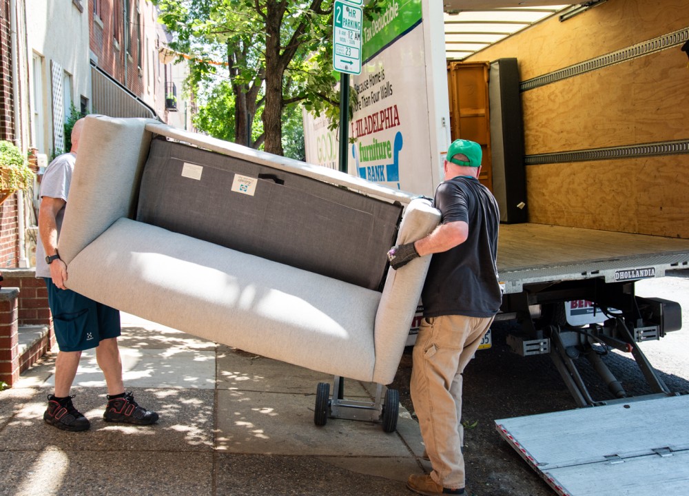 two movers carrying couch onto truck
