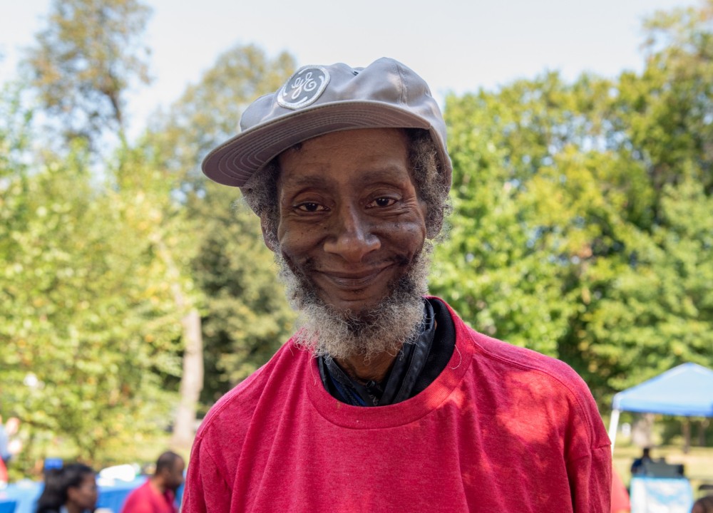 participant smirking at camera outside, trees in background