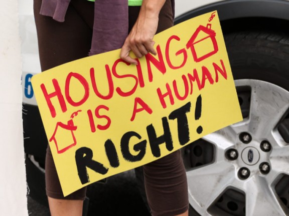 hand holding a sign reading "housing is a human right!"