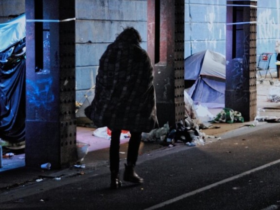 man walking past tents under an overpass