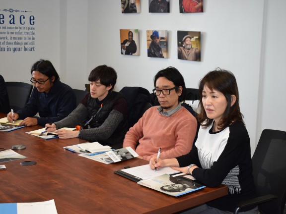 several visitors sit at a conference table, taking notes during a site visit