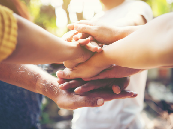 Several people stacking their hands together in a gesture of unity and support, with soft natural light in the background