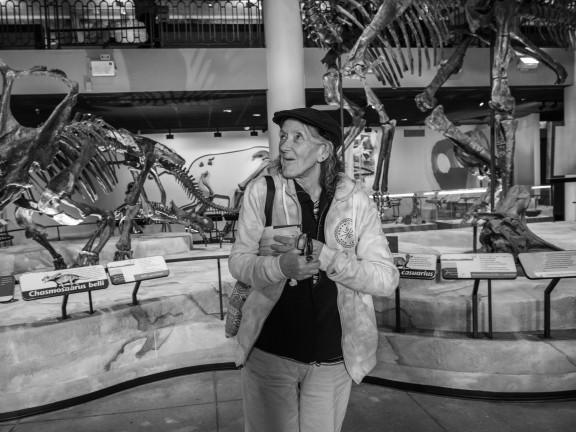 A smiling woman stands in front of dinosaur bones at a museum
