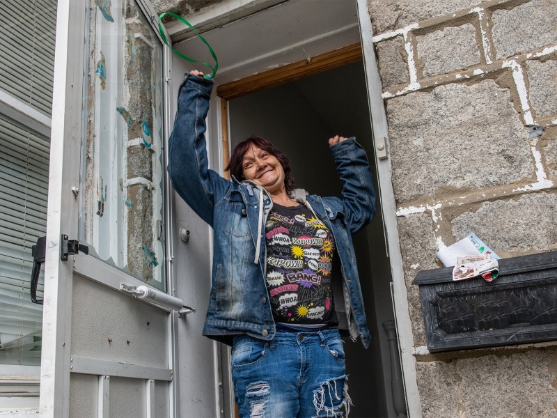 woman with hands in the air, happy, holding her keys in front of her home