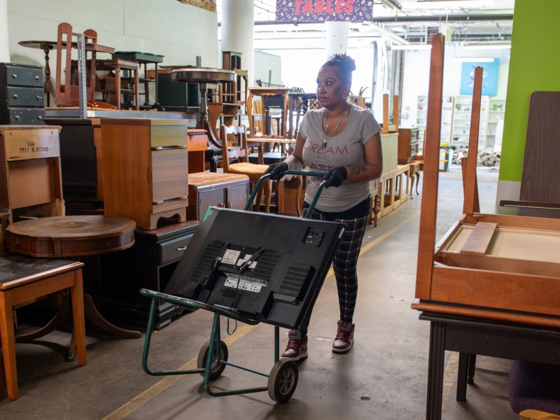 Ednara pushing a tv on a dolly in the Furniture Bank