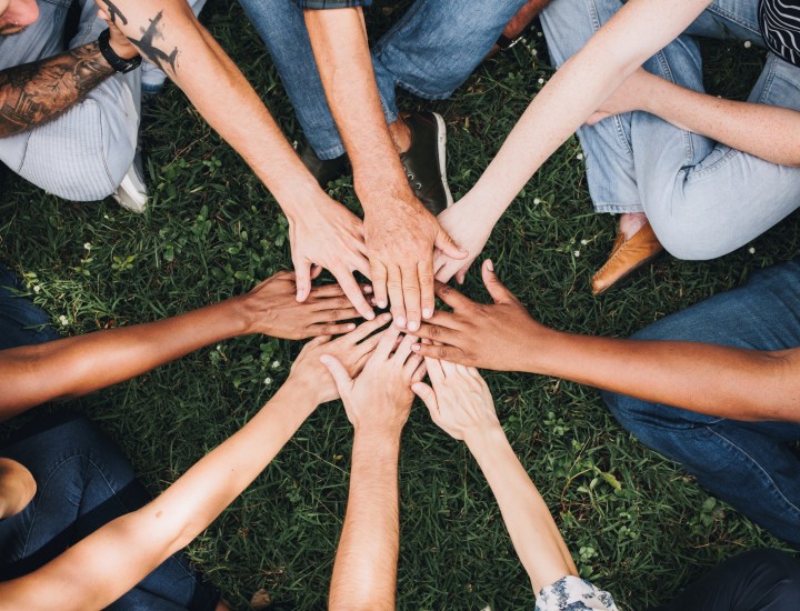 folks of different ethnicities stacking hands together, sitting in a circle