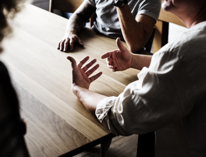 three people seated at a table with dark shadows, they are conversating