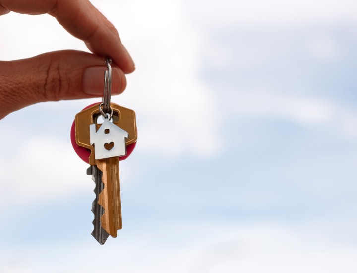 hand holding keys outdoors, sky background, keys on keyring with house charm