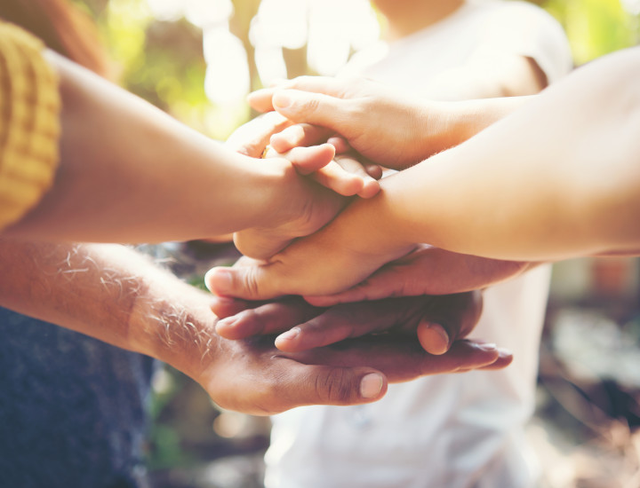 Several people stacking their hands together in a gesture of unity and support, with soft natural light in the background