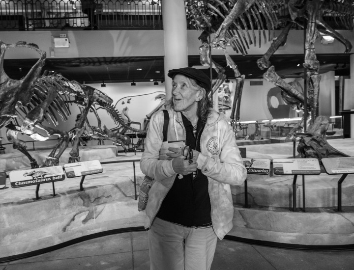 A smiling woman stands in front of dinosaur bones at a museum